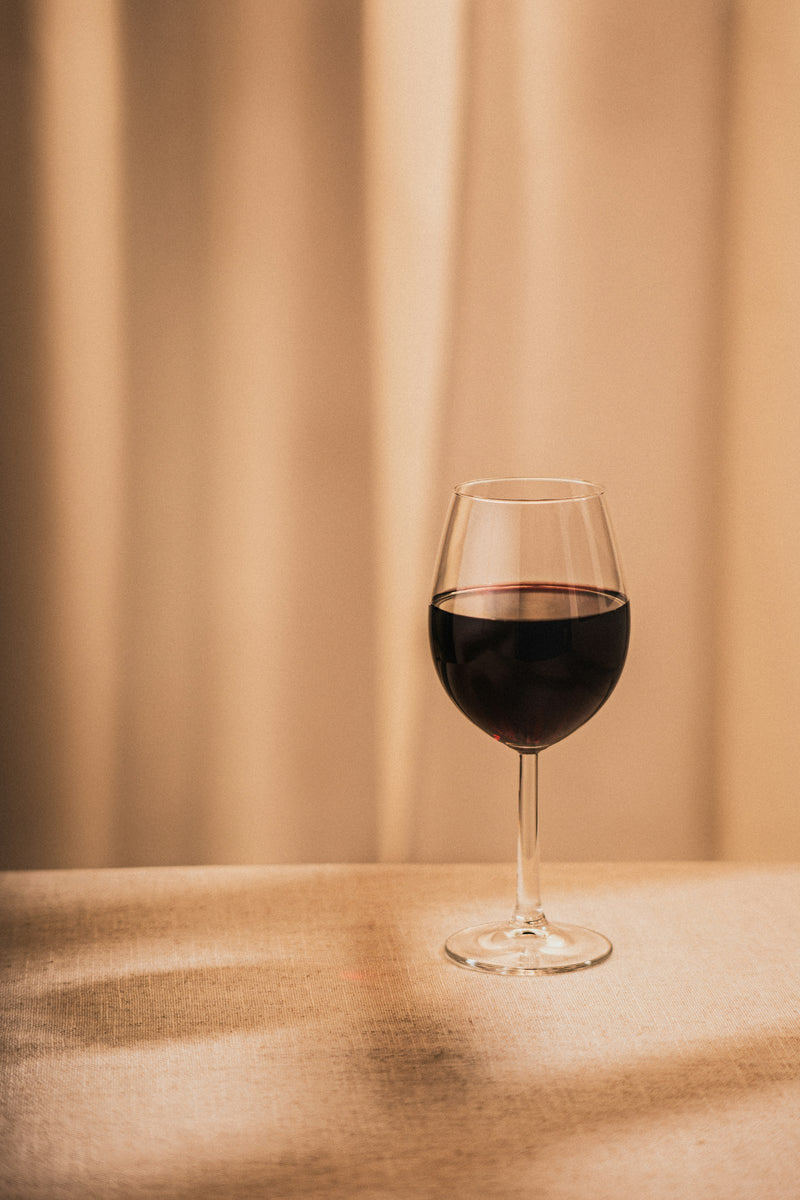 Weinglas mit Rotwein vor beigem Vorhang